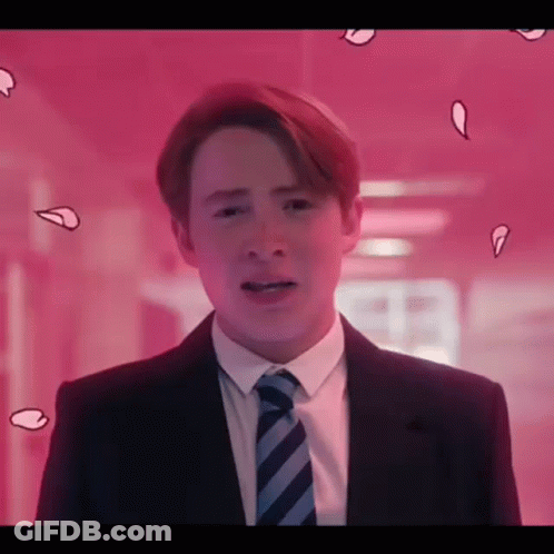 A Young Man In A Suit And Tie Is Standing In Front Of A Pink Wall . GIF