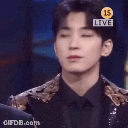 A Young Man In A Suit And Tie Is Standing In Front Of A Sign That Says `` Live '' . GIF
