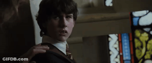 A Young Man In A Suit And Tie Is Standing Next To A Stained Glass Window . GIF