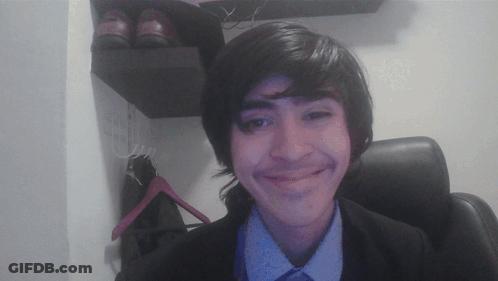 A Young Man In A Suit And Tie Smiles In Front Of A Pair Of Shoes GIF