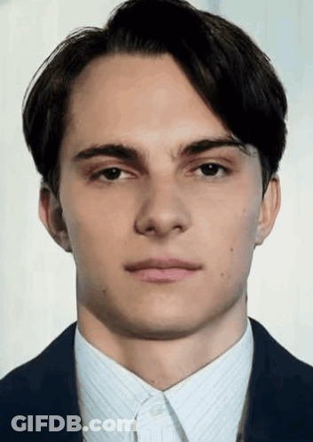 A Young Man In A Suit And White Shirt Looks At The Camera With A Serious Look On His Face GIF