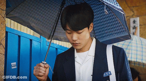 A Young Man In A Suit Is Holding A Blue Umbrella . GIF