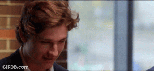 A Young Man In A Suit Is Sitting In Front Of A Window And Smiling . GIF