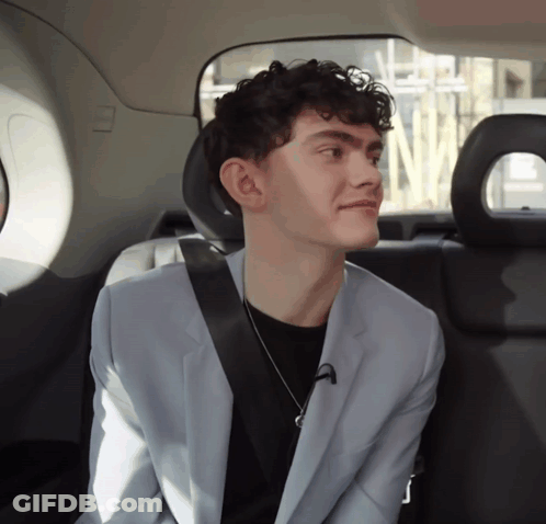 A Young Man In A Suit Is Sitting In The Back Seat Of A Car GIF