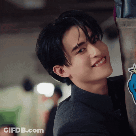 A Young Man In A Suit Is Smiling While Leaning Against A Wall With A Blue Star On It GIF