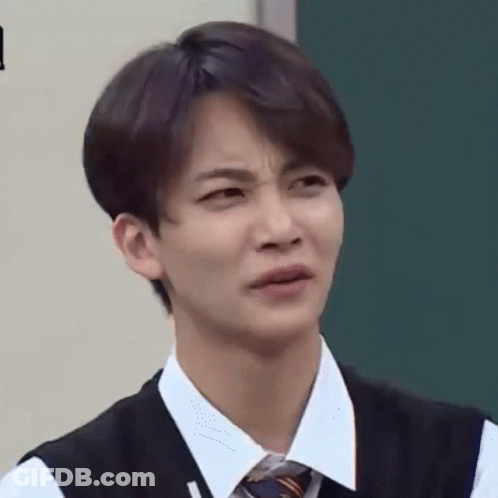 A Young Man In A Vest And Tie Is Making A Funny Face In Front Of A Blackboard . GIF