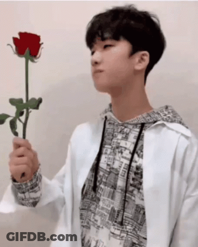 A Young Man In A White Jacket Holds A Red Rose In His Hand GIF