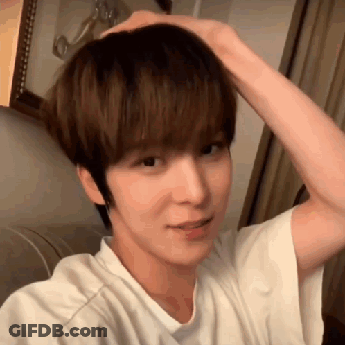 A Young Man In A White Shirt Is Holding His Hair In His Hand . GIF
