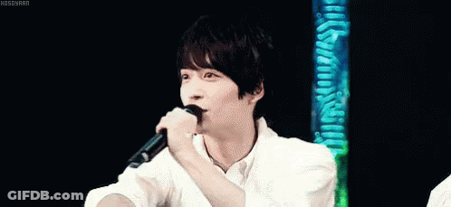 A Young Man In A White Shirt Is Holding His Hand To His Forehead . GIF