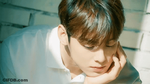 A Young Man In A White Shirt Is Laying Down With His Hand On His Face . GIF