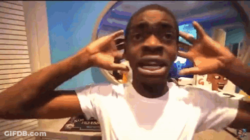 A Young Man In A White Shirt Is Making A Funny Face With His Hands . GIF