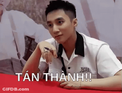 A Young Man In A White Shirt Is Sitting At A Table With His Hand On His Chin . GIF
