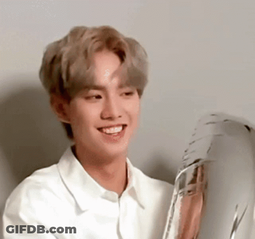 A Young Man In A White Shirt Is Smiling And Holding A Balloon . GIF