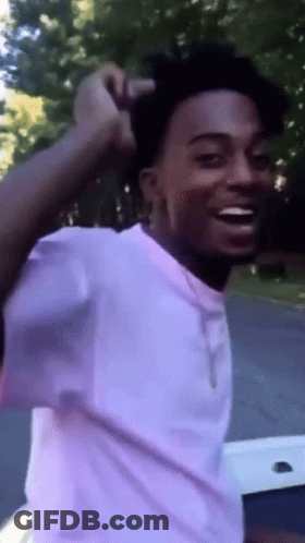 A Young Man In A White Shirt Is Smiling And Holding His Hair GIF