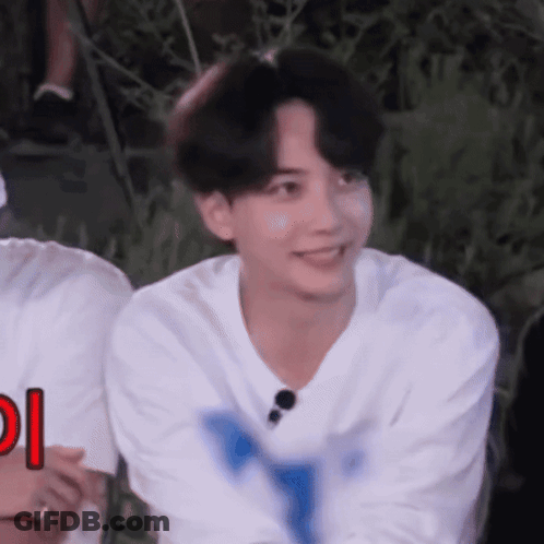 A Young Man In A White Shirt Is Smiling And Looking At The Camera While Sitting In A Chair . GIF