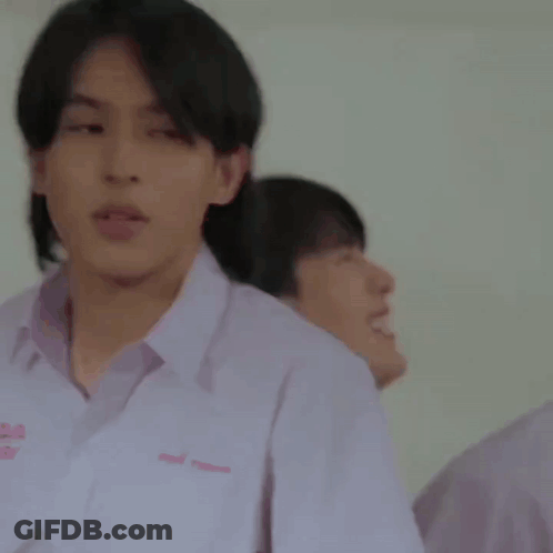 A Young Man In A White Shirt Is Standing In Front Of A Blackboard . GIF