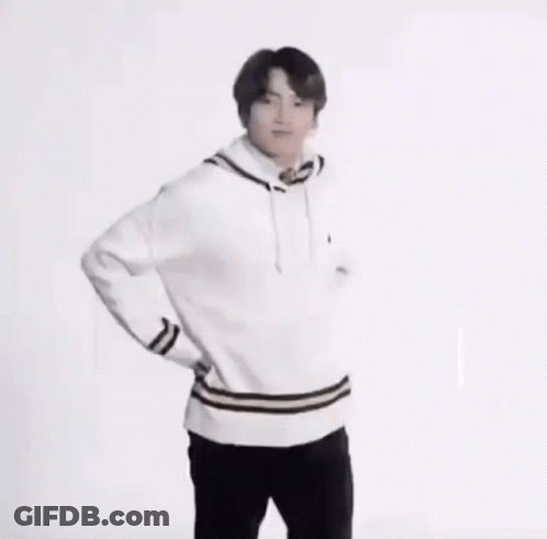 A Young Man In A White Sweater And Black Pants Is Standing With His Hands On His Hips And Smiling . GIF