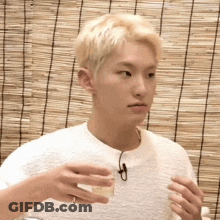 A Young Man In A White Sweater Is Holding A Cup Of Coffee In His Hand . GIF
