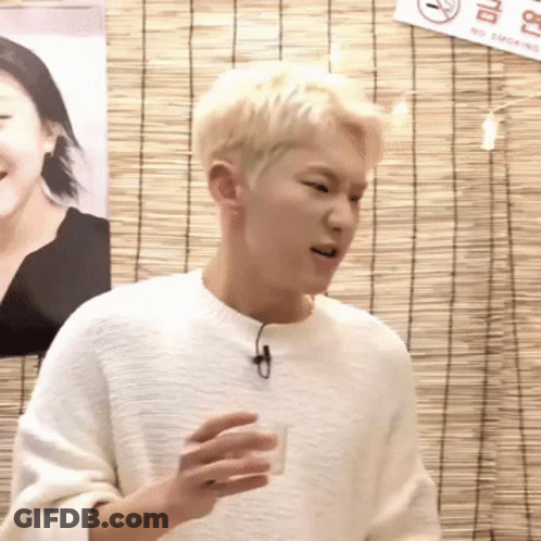 A Young Man In A White Sweater Is Holding A Shot Glass In Front Of A No Smoking Sign . GIF