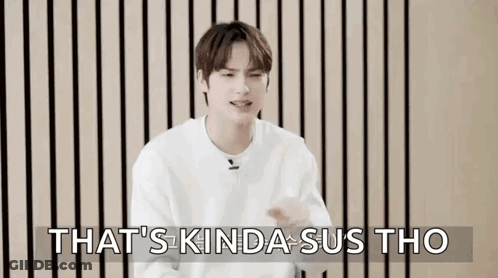 A Young Man In A White Sweater Is Sitting In Front Of A Wooden Wall And Making A Funny Face . GIF