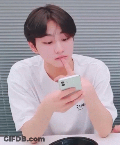 A Young Man In A White T-Shirt Is Looking At A Cell Phone GIF
