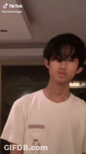 A Young Man In A White T-Shirt Is Standing In A Room . GIF