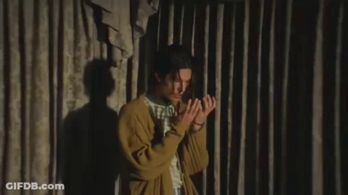 A Young Man In A Yellow Cardigan Is Making A Funny Face While Sitting In Front Of A Curtain . GIF