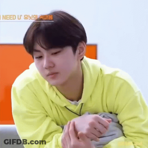 A Young Man In A Yellow Hoodie Is Sitting On A Couch With His Hands Folded . GIF
