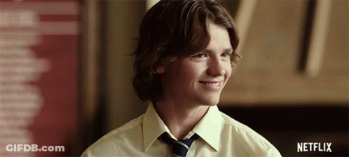 A Young Man In A Yellow Shirt And Tie Is Smiling With A Netflix Logo In The Background GIF