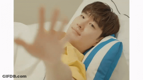 A Young Man In A Yellow Shirt Is Laying In Bed With A Blue And White Striped Pillow GIF