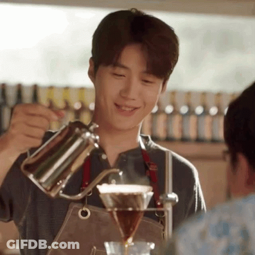 A Young Man In An Apron Is Pouring Coffee Into A Glass . GIF