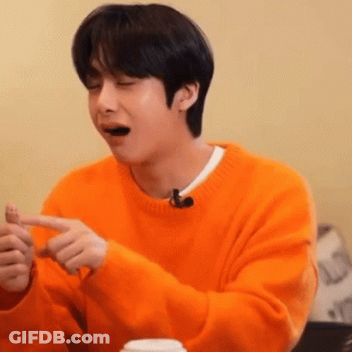 A Young Man In An Orange Sweater Is Sitting At A Table With His Eyes Closed And His Mouth Open . GIF