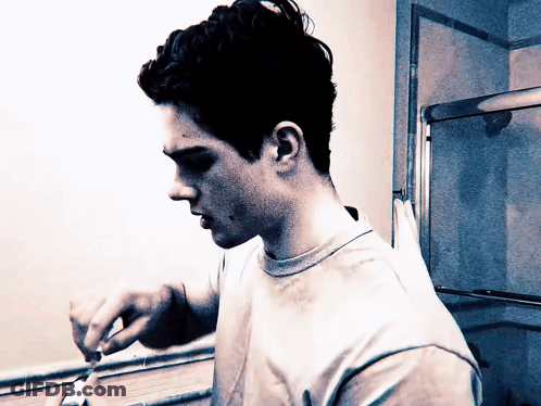 A Young Man Is Brushing His Teeth In Front Of A Bathroom Mirror GIF