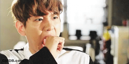 A Young Man Is Covering His Mouth With His Hand While Looking At The Camera . GIF