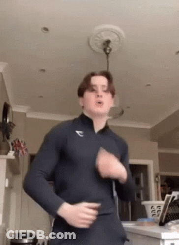 A Young Man Is Dancing In A Living Room While Wearing A Blue Shirt . GIF