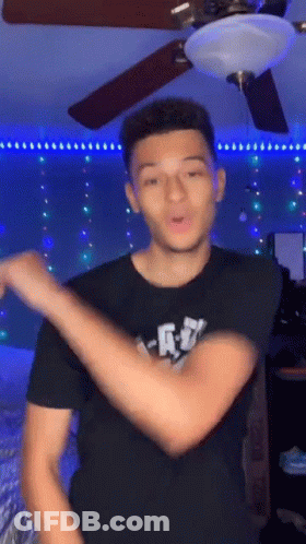 A Young Man Is Dancing In A Room With A Ceiling Fan And A Light . GIF