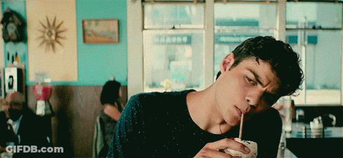 A Young Man Is Drinking A Milkshake Through A Straw In A Restaurant . GIF