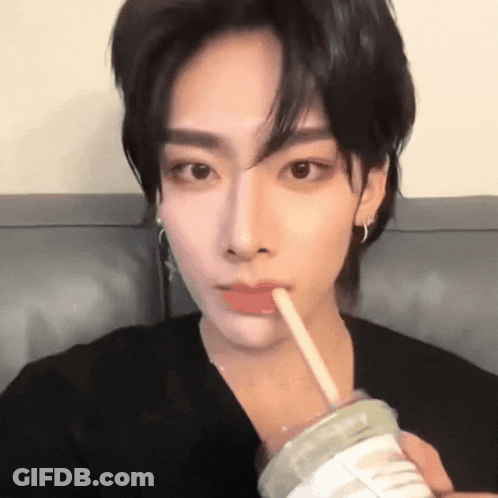 A Young Man Is Drinking From A Cup With A Straw In His Mouth . GIF