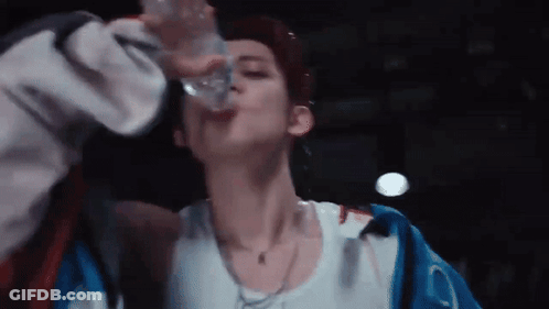 A Young Man Is Drinking Water From A Bottle . GIF