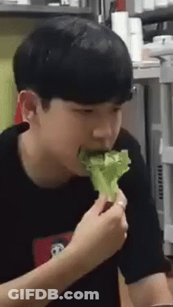 A Young Man Is Eating A Piece Of Lettuce From A Plate . GIF