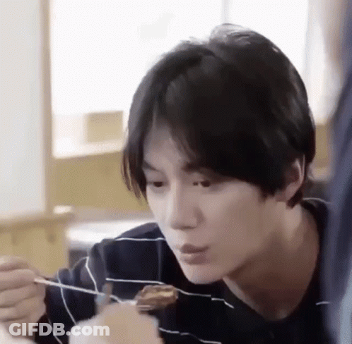A Young Man Is Eating Food With A Fork And Spoon . GIF