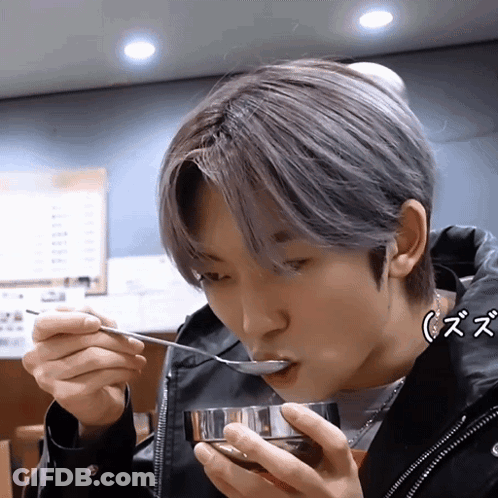 A Young Man Is Eating From A Bowl With A Spoon While Wearing A Black Jacket GIF