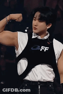 A Young Man Is Flexing His Muscles On A Stage While Wearing A Black Vest . GIF