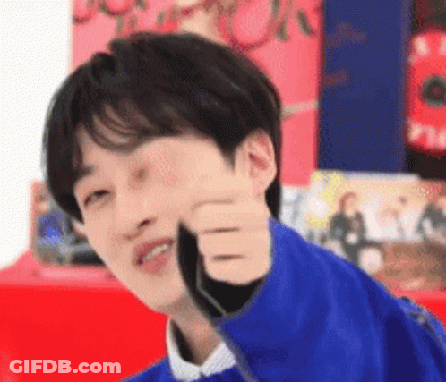 A Young Man Is Giving A Thumbs Up Sign While Wearing A Blue Jacket . GIF