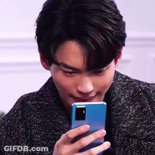 A Young Man Is Holding A Blue Cell Phone In His Hand And Looking At It . GIF