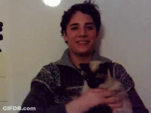 A Young Man Is Holding A Cat In His Arms And Smiling GIF