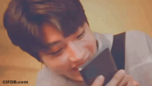 A Young Man Is Holding A Cell Phone In His Hand And Smelling It . GIF