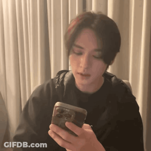 A Young Man Is Holding A Cell Phone In His Hand . GIF