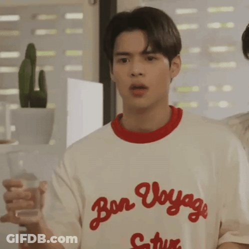 A Young Man Is Holding A Glass Of Water While Wearing A T-Shirt That Says Bon Voyage . GIF