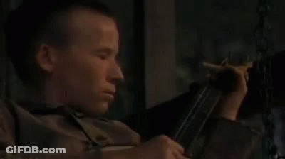 A Young Man Is Holding A Gun And Smoking A Cigarette . GIF